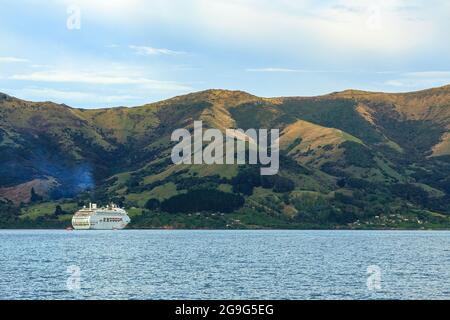 Una grande nave da crociera nel porto di Akaroa, Nuova Zelanda, dwarfed da una serie di montagne costiere Foto Stock