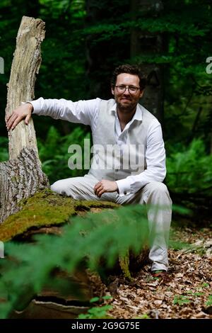 Mittelangeln, Germania. 26 luglio 2021. Jan Philipp Albrecht (Bündnis 90/Die Grünen), Schleswig-Holstein Ministro per la transizione energetica, l'agricoltura, l'ambiente, la natura e la digitalizzazione siede su un tronco d'albero. Albrecht segnò l'albero dell'habitat del 80000. Gli alberi sono indispensabili per la conservazione e la promozione della biodiversità e la conservazione della natura delle foreste integrative, hanno spiegato i rappresentanti delle foreste statali dello Schleswig-Holstein in occasione di un evento stampa. Credit: Frank Molter/dpa/Alamy Live News Foto Stock