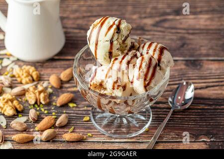 Gelato di mandorle, pistacchio e noce Roma in una ciotola di vetro con salsa al caramello. Foto Stock