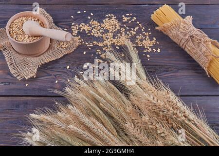 Vista dall'alto grani di grano con macinacaffè e spaghetti su legno scuro. Foto Stock