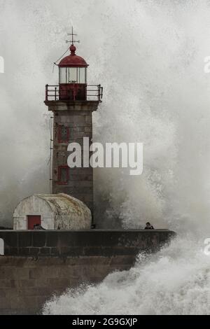 Porto, Portogallo - 7 febbraio 2016: Grandi onde oceaniche contro il vecchio faro e molo in un pomeriggio tempestoso vedere le persone in fuga. Foto Stock