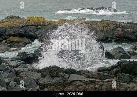 Onde e spruzzi che si schiantano contro le rocce Foto Stock