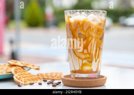 Caffè latte al caramello ghiacciato in un bicchiere alto con caramello sciroppo Foto Stock