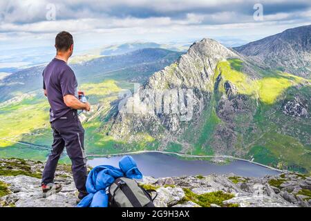 Snowdonia, Regno Unito. 14 luglio 2021. Con un numero sempre maggiore di persone in vacanza nel Regno Unito, la catena montuosa Snowdonia offre una vista mozzafiato per coloro che desiderano una vacanza all'insegna dell'avventura. Un escursionista mostrato qui dopo aver raggiunto la cima di Pen yr Ole Wen godendo delle viste gloriose mentre guarda giù nella valle al lago Ogwen e fino a Tryfan. Credito: Lee Hudson Foto Stock