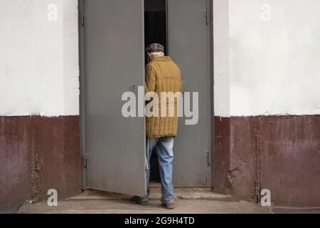 Il vecchio cammina nella porta. Un uomo anziano entra nell'ingresso della casa. Un pensionato entra in un edificio di appartamenti. Foto Stock