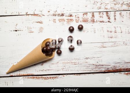 Praline di cioccolato in cono di carta su tavola di legno. Foto Stock