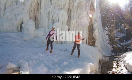 Colpo a mano di un paio caucasico, scalatori di ghiaccio in abiti protettivi ai piedi della cascata ghiacciata in preparazione per la prossima salita Foto Stock