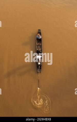 Vista aerea un pescatore asiatico si erge su una tradizionale barca da pesca in legno mentre si gettano reti da pesca su un fiume all'alba. Scena rurale in Thailandia. Foto Stock