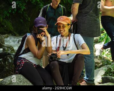 Amaga, Antioquia, Colombia - Luglio 18 2021: Donne ispaniche che siedono sulle rocce sulla Riverbank che scattano foto nel mezzo della natura Foto Stock
