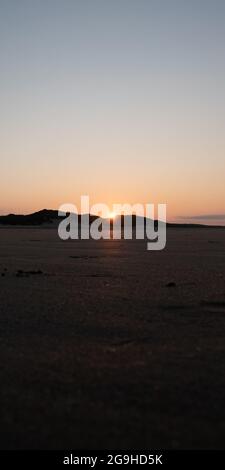 Sole ambientazione dietro dune di sabbia che riflettono una bella e ricca luce arancione sulla sabbia Foto Stock