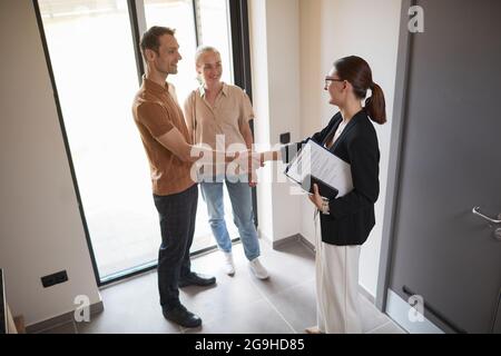 Ritratto ad alto angolo di giovane coppia che scuote le mani con agente immobiliare durante il tour dell'appartamento, spazio per la copia Foto Stock