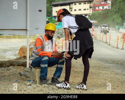 Amaga, Antioquia, Colombia - Luglio 18 2021: Giovane donna Latina in Sportswear chiede il numero di telefono di un uomo che indossa una maschera nera, cappello giallo e duro Foto Stock