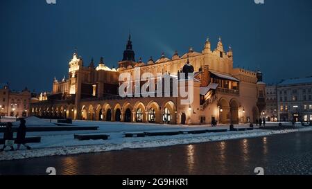 Cracovia, Polonia 03.02.2021 Vista notturna del Palazzo dei tessuti e del Municipio di Cracovia situato al centro della piazza principale del mercato nella Città Vecchia di Cracovia, Polonia. Strada innevata durante la stagione invernale. Cielo blu chiaro. Foto Stock