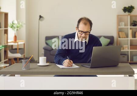 Uomo maturo seduto davanti allo schermo del computer portatile scrivendo su un ritratto del notebook cartaceo Foto Stock