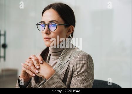 Donna di charme focalizzata in occhiali pensando mentre lavorando in ufficio Foto Stock