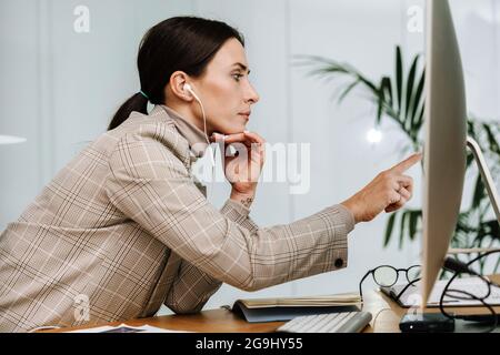 Donna seria negli auricolari che usa lavorare con il computer in ufficio Foto Stock