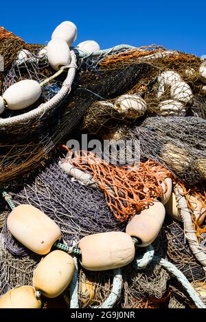 Una collezione di attrezzi da pesca commerciali in deposito sotto un cielo blu. Le corde per un modello ripetitivo contro reti e galleggianti Foto Stock