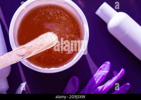 Pasta di zucchero per la rimozione dei capelli. Primo piano della pasta Shugaring. Lo zucchero liquido scorre giù una spatola di legno. Abbagliamento del sole. Vista dall'alto Shugarig Set. Foto Stock