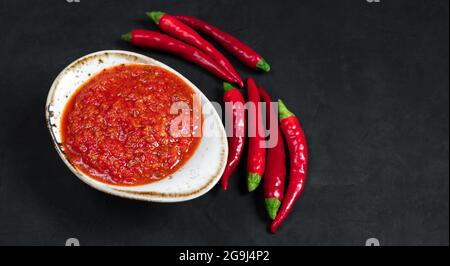 Incolla la salsa di harissa in una ciotola su un closeup nero di fondo. Adjika salsa piccante di peperoni. Spazio di copia. Foto Stock