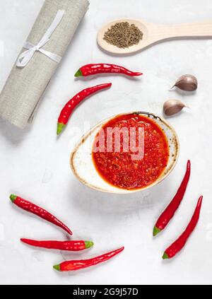 Pasta Harissa. Salsa al peperoncino piccante su fondo bianco. Adjika in un recipiente con peperoncino, aglio e spezie. Orientamento verticale. Vista dall'alto. Foto Stock