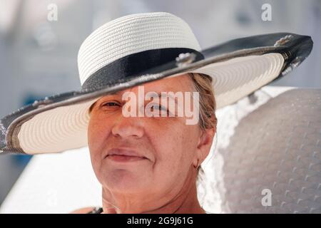 Una donna in un cappello di paglia. Ritratto in primo piano di una donna adulta sorridente in un cappello di paglia bianca in una giornata di sole brillante Foto Stock