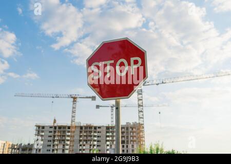 Vecchio cartello rosso di stop di fronte a un cantiere con gru alte Foto Stock