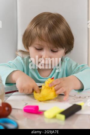 Una ragazza di tre anni in una blusa turchese sta facendo con entusiasmo un pollo giallo al tavolo Foto Stock