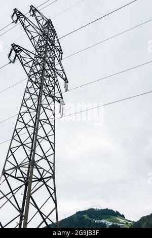 Linea elettrica aerea ad alta tensione, pilone elettrico, torre in acciaio che si erge sulle Alpi e parco solare, centrale fotovoltaica situata o Foto Stock