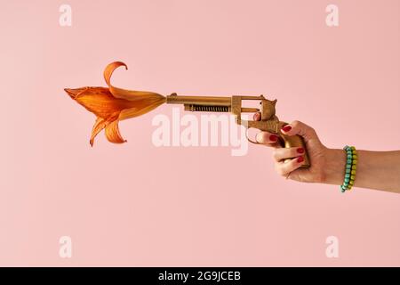 La mano della donna spara da una falsa pistola dipinta d'oro di cui un fiore sta uscendo Foto Stock