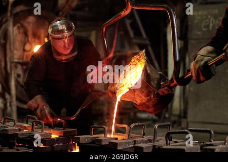 I lavoratori in caschi che lavorano in squadra si fondono il ferro dentro fabbrica di metallo Foto Stock