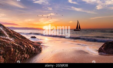 Una barca a vela sta navigando lungo l'oceano con un gregge di uccelli che volano sopra UN cielo colorato di tramonto Foto Stock