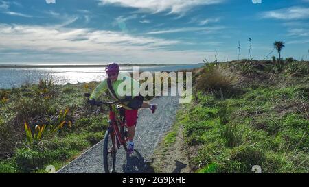 Una donna di mezza età (65) si smonta da una bicicletta elettrica in un giro attraverso l'estuario di Waikanae, Nuova Zelanda. Foto Stock