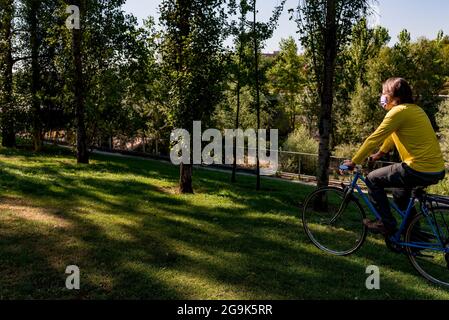 Uomo che indossa una maschera al parco con la sua bicicletta Foto Stock