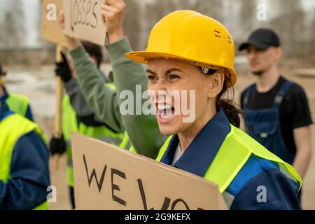 Molto arrabbiato donna costruttore e i suoi colleghi con cartelli che gridano sullo sciopero Foto Stock