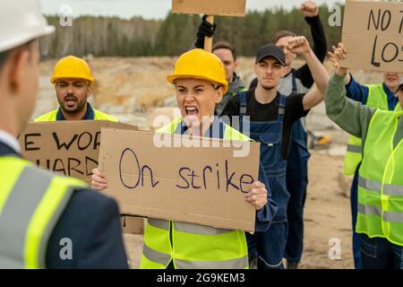 Feroce donna e altri lavoratori in cava che trasportano cartelli di fronte al proprio datore di lavoro Foto Stock