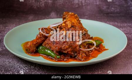 Pollo cotto in curry rosso secco speziato guarnito con anello di cipolla e peperoncino verde. Foto Stock