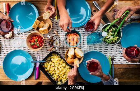 Vista dall'alto del tavolo pieno di cibo e riends godendo l'evento insieme - piatti blu e sfondo colorato - concetto di no coronavirus famiglia e amici Foto Stock