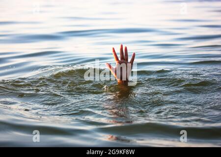 Un uomo sta annegando in acqua. Una mano sbirciata da sotto un'acqua. Una persona affogata ha bisogno di aiuto, soccorso. Un rischio, pericolo di vivere in mare, fiume, oc Foto Stock