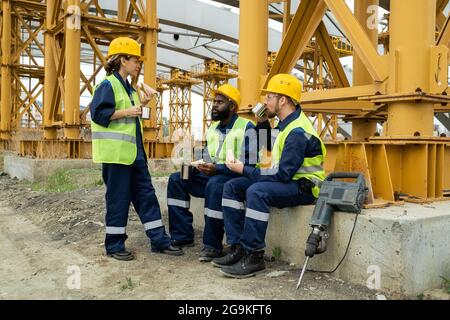 Gruppo di lavoratori edili che bevono caffè e si comunicano tra loro durante la pausa caffè all'aperto Foto Stock