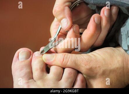 Master in manicure nel processo di lavoro rifilatura cuticole sulle dita dei piedi con forbici per pedicure, taglienti per unghie in pezzatura. Vista mani e piedi da vicino. Centro benessere diurno. Foto Stock