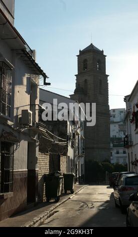 Stretta strada del villaggio che conduce alla chiesa parrocchiale fiancheggiata da automobili e contenitori per rifiuti Foto Stock