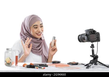 Blogger di bellezza in hijab tenendo una bottiglia di rossetto registrare video con la macchina fotografica Foto Stock