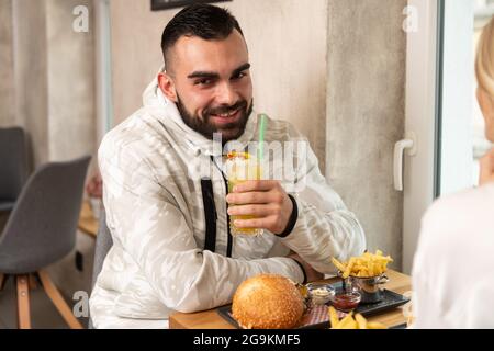 Ritratto di giovane coppia mangiare hamburger al ristorante e cocktail Passione frutta Mojito Foto Stock