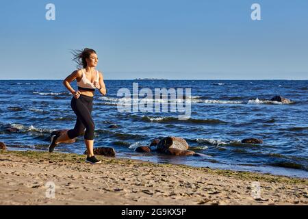 Donna bianca di 30 anni corre sulla spiaggia di giorno. Foto Stock