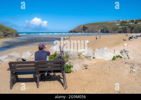 Spiaggia di Mawgan Porth in Cornovaglia; un camminatore riposato su una panchina di legno che si affaccia sulla spiaggia e godendo il sole. Foto Stock