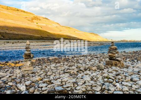 Coppia di cairns di rocce impilate sulla riva con una collina accanto all'acqua sullo sfondo Foto Stock