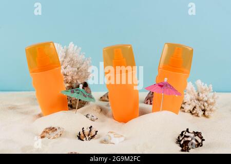 bottiglie arancioni di crema solare vicino alle conchiglie sulla sabbia isolata su blu Foto Stock