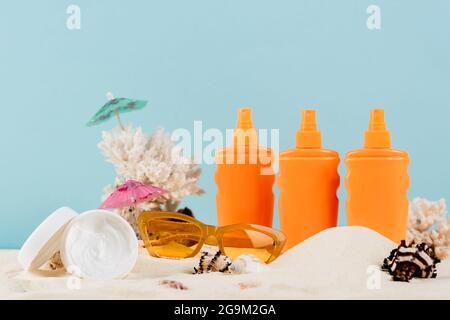 contenitori con crema solare e cosmetici vicino occhiali da sole su sabbia isolata su blu Foto Stock