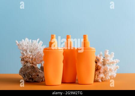bottiglie arancioni di crema solare vicino ai coralli marini isolati su blu Foto Stock