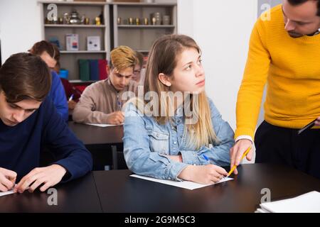 Grave giovane insegnante dare spiegazione agli studenti durante il lavoro di revisione in classe Foto Stock